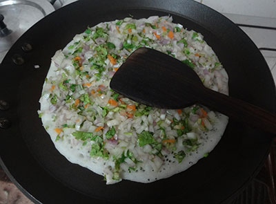 preparing onion dosa or onion uttappam