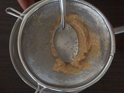 straining the ground paste for southe beejada saru or cucumber seeds rasam